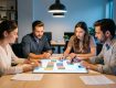 Quatre fondateurs, deux femmes et deux hommes, réunis autour d’une table avec des documents financiers vierges et un tableau de stratégie lumineux.